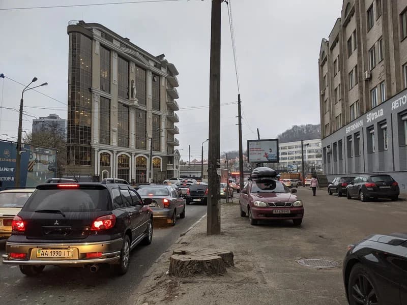 Бізнес-центр “Гефест”, автомобільний затор, пеньок зрізаного дерева і автомобілі, припарковані на тротуарі на вулиці Глибочицькій у Києві, 2021